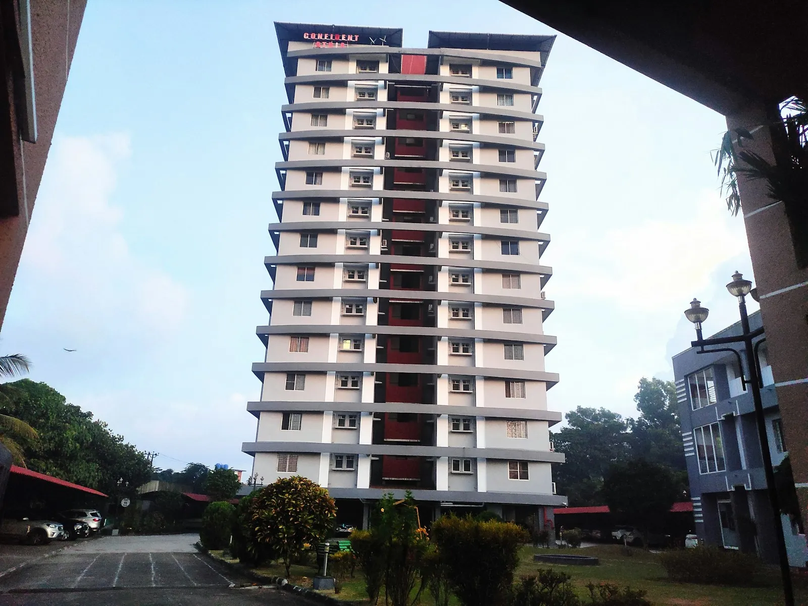 A white residential tower with balconies on every floor, trees in front